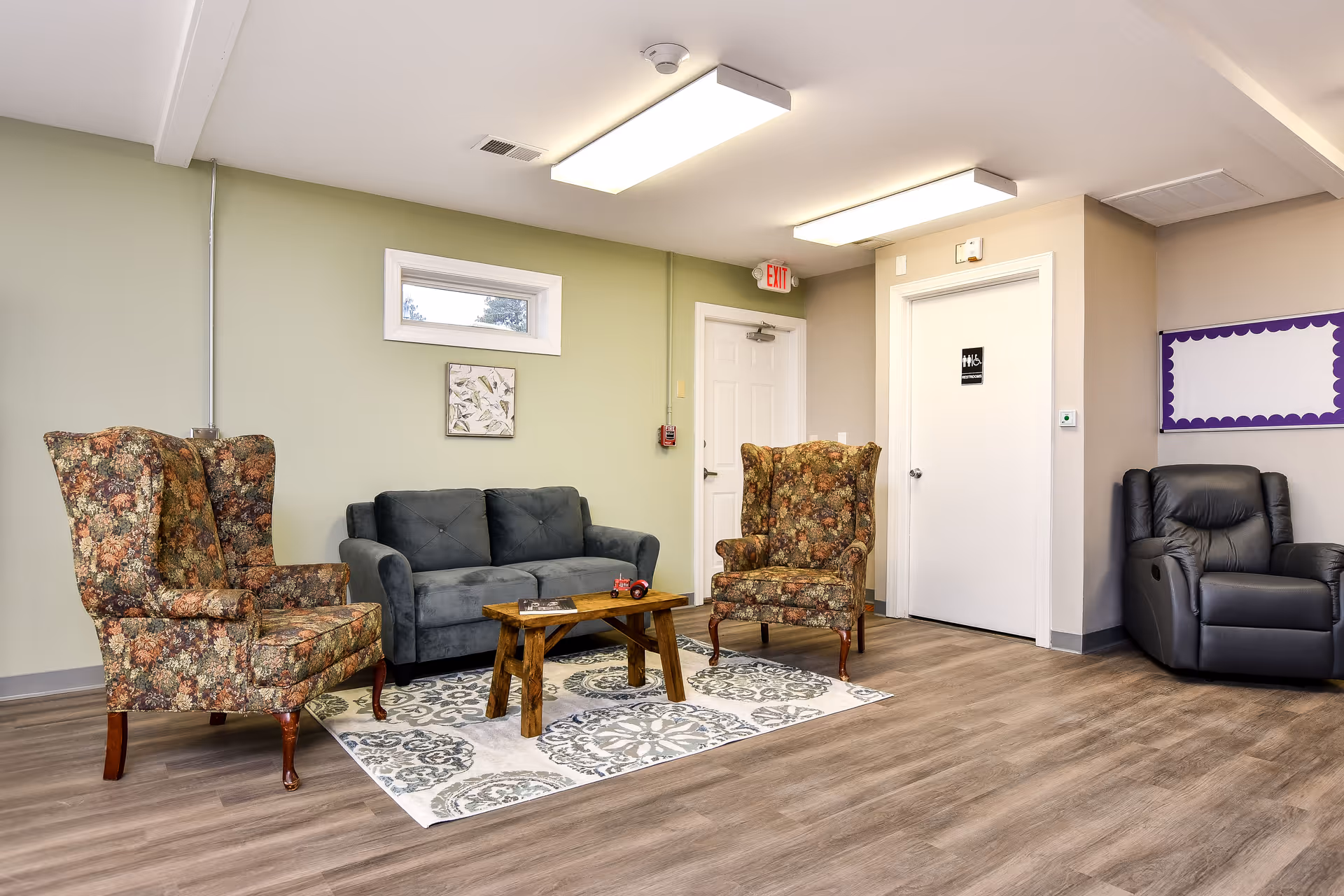 Lounge area with floral armchairs, a blue sofa, wooden coffee table, rug, and exit door.