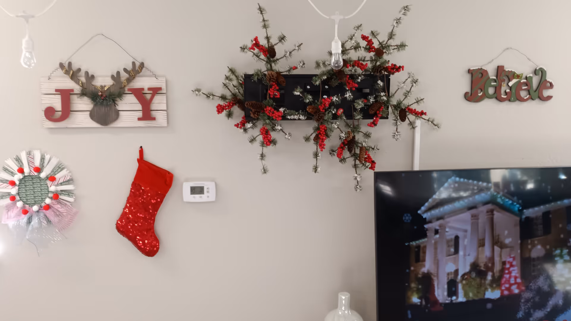 Decorated wall with a JOY sign, stockings, wreath, and a TV in a cozy common area.