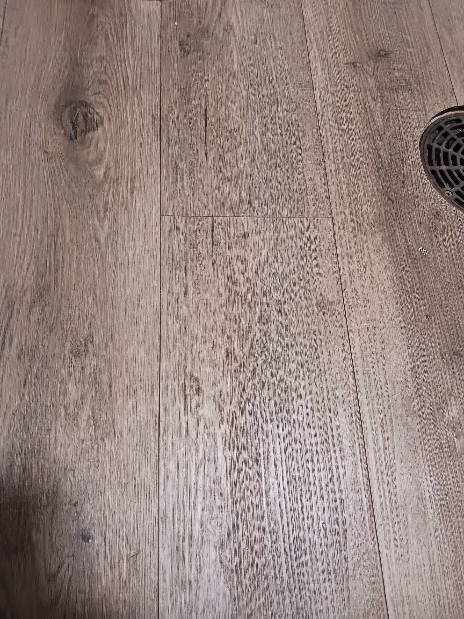 Wooden floor planks with a round drain near the edge.