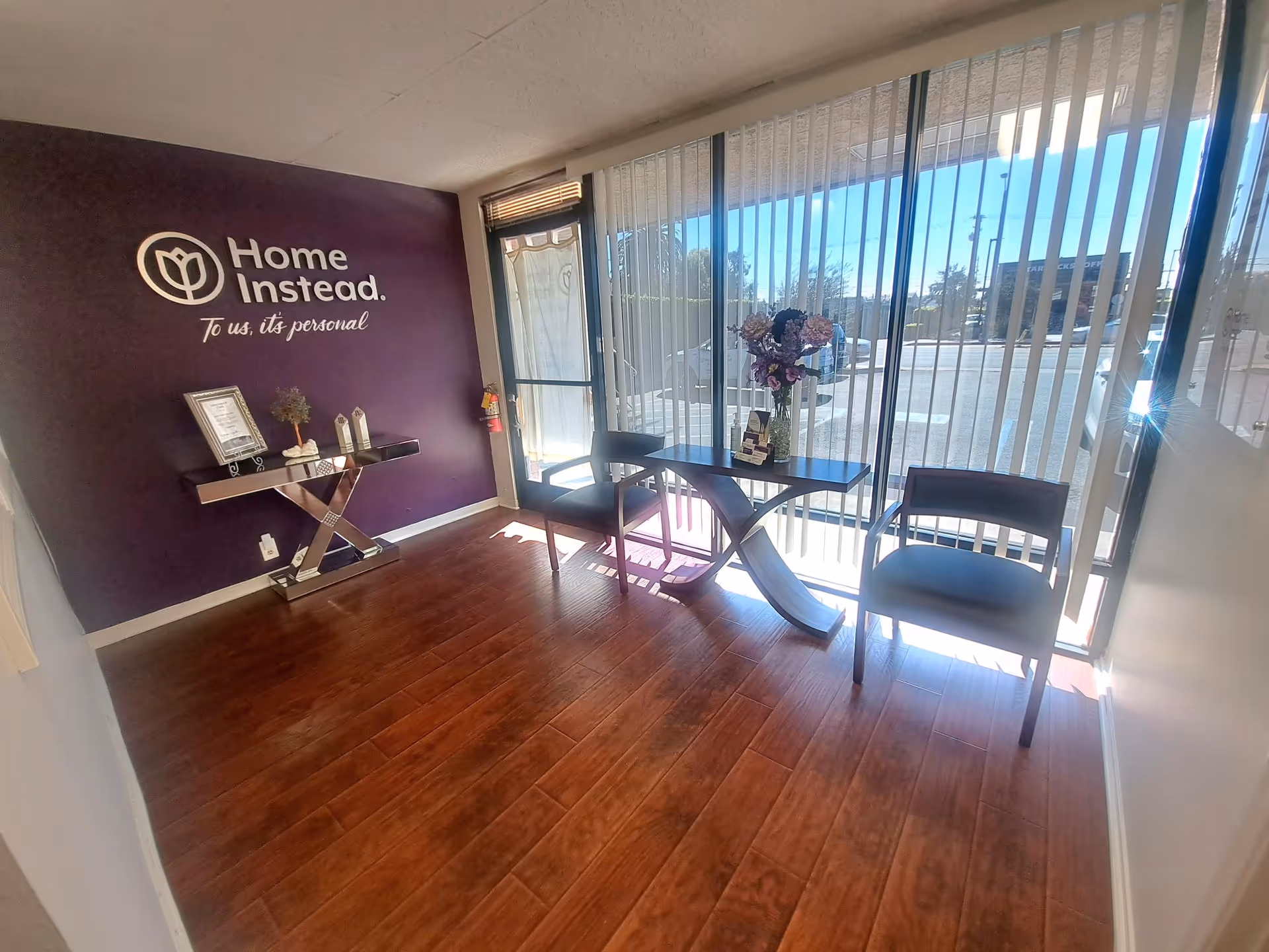 Lobby area of Home Instead with purple wall logo, windows, and seating.