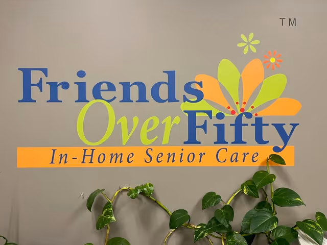 Wall sign reads Friends Over Fifty In-Home Senior Care with colorful logo; potted plants below.