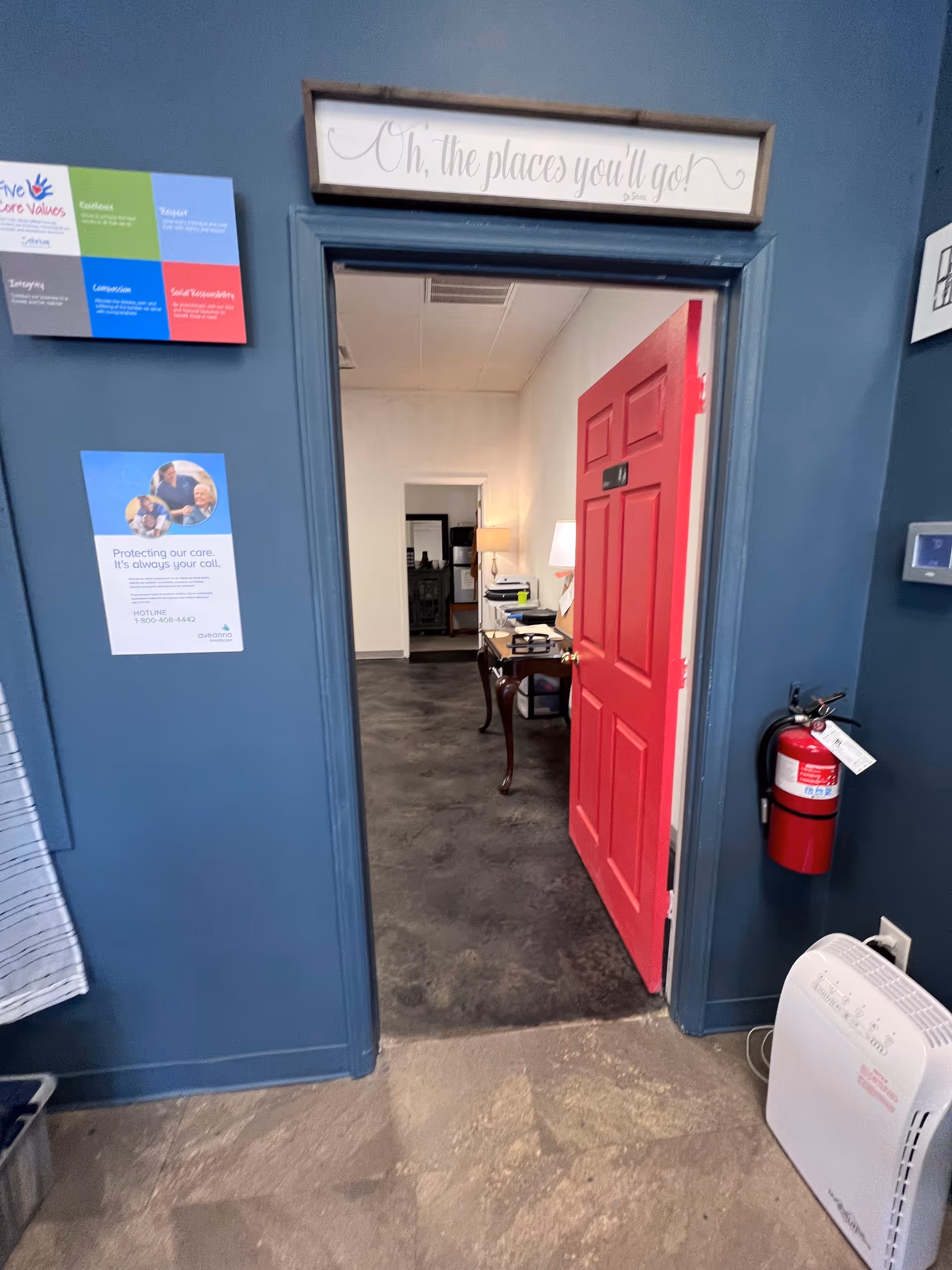 Open red door leads to a small office in a blue-walled interior hallway.