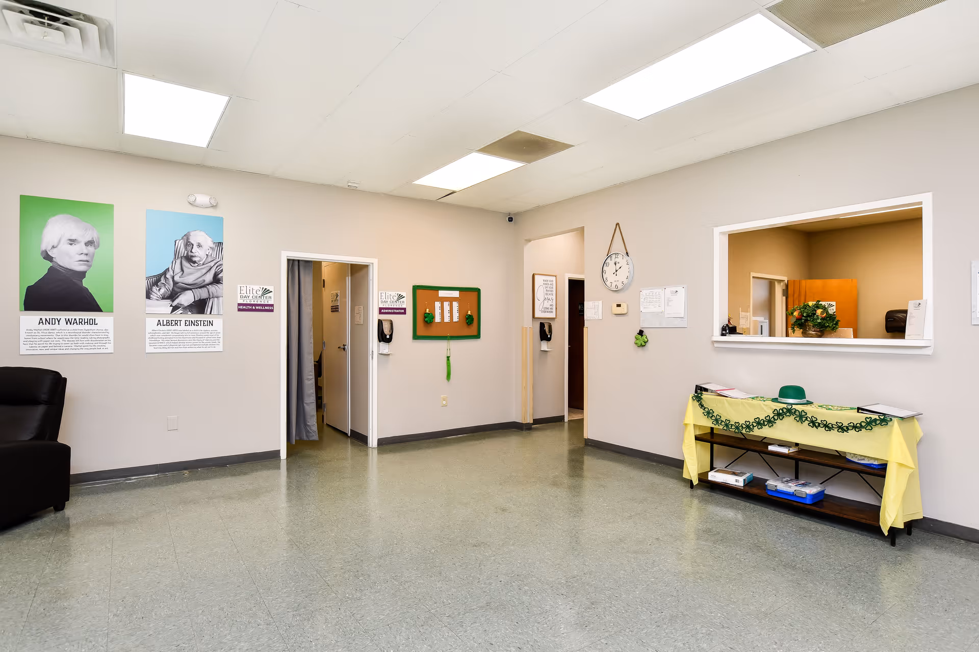 Bright lobby area with a reception window, posters on wall, and a table covered with cloth.