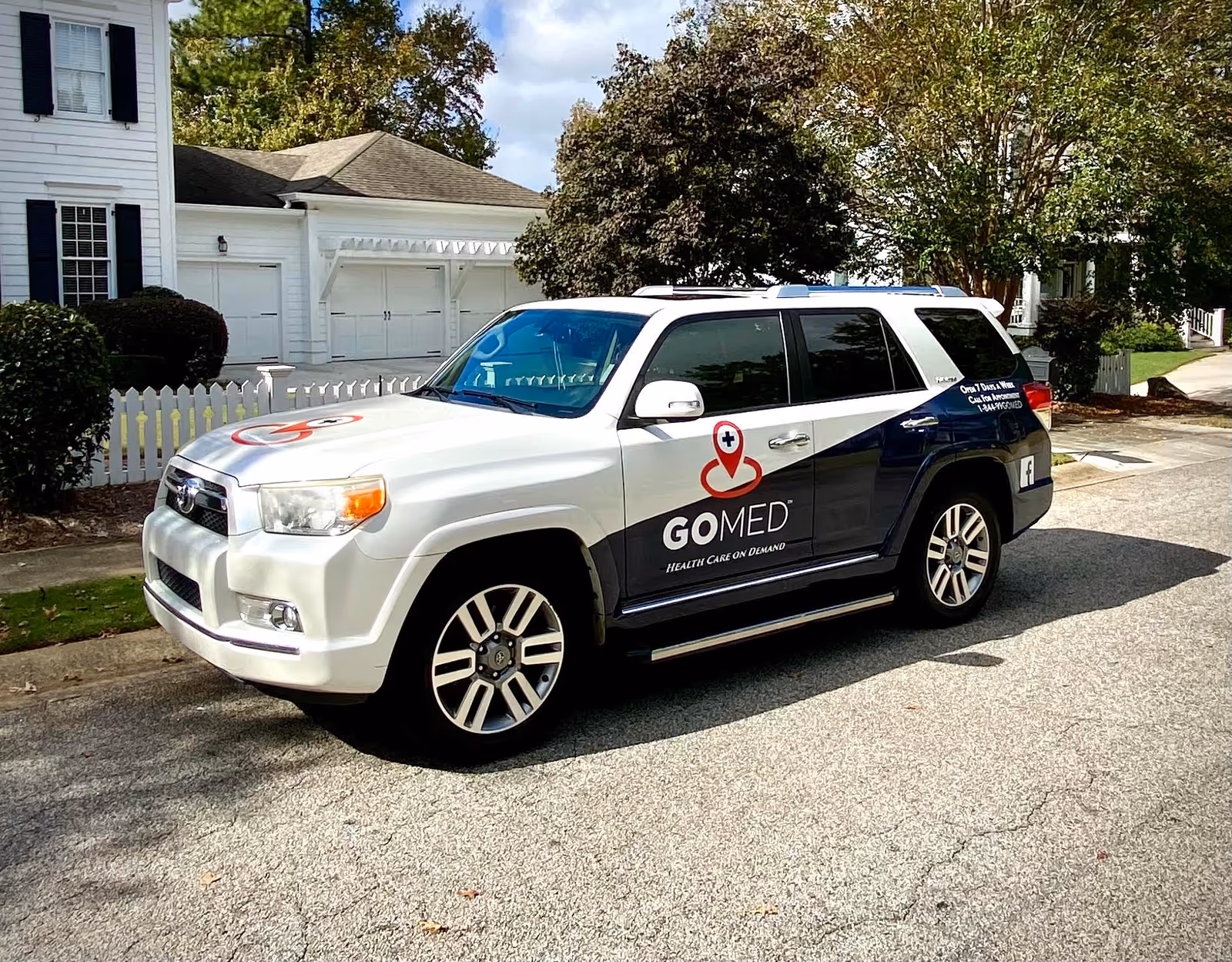 GOMED mobile urgent care SUV parked on a suburban street beside a white house.
