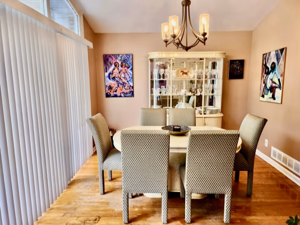 Bright dining room with a round table, eight upholstered chairs, china cabinet, and chandelier.