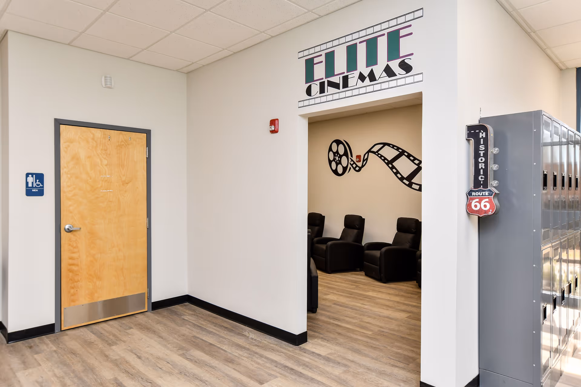 Interior hallway to Elite Cinemas with black seating visible and an accessibility door sign.