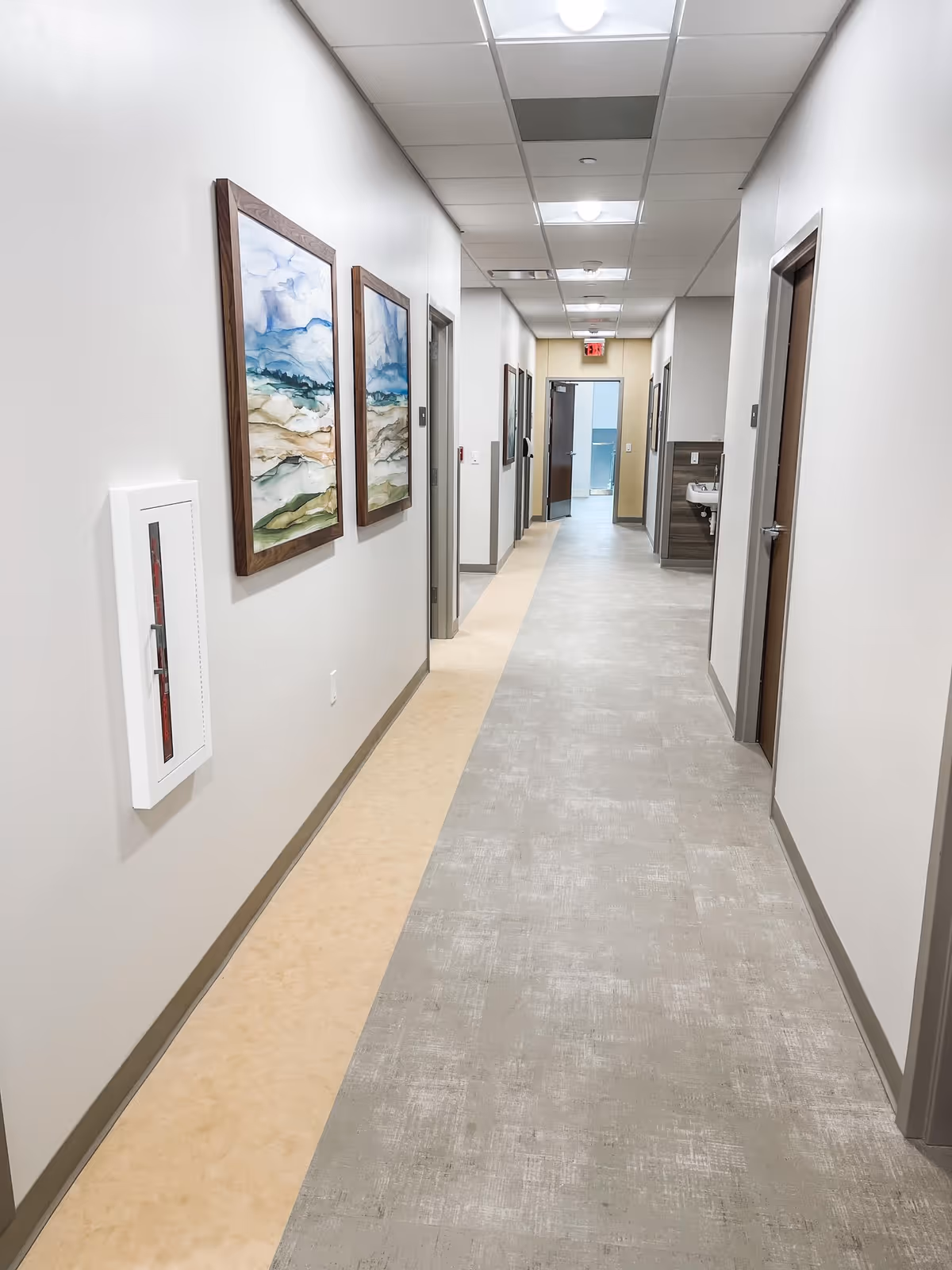 Long hallway in a senior living facility with framed artwork and multiple doors.