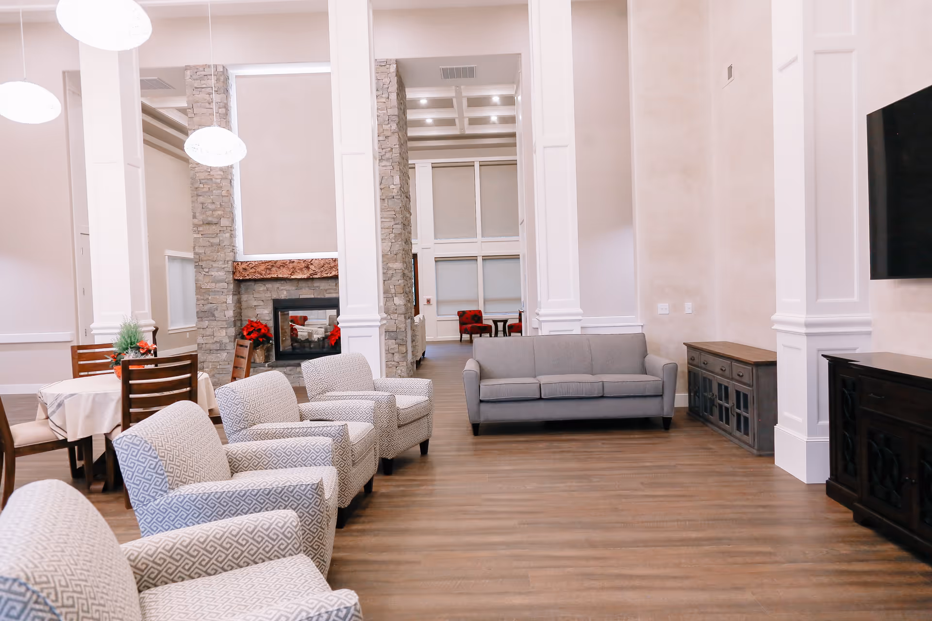 Bright senior living lounge with sofas, chairs, fireplace, and a wall-mounted TV.