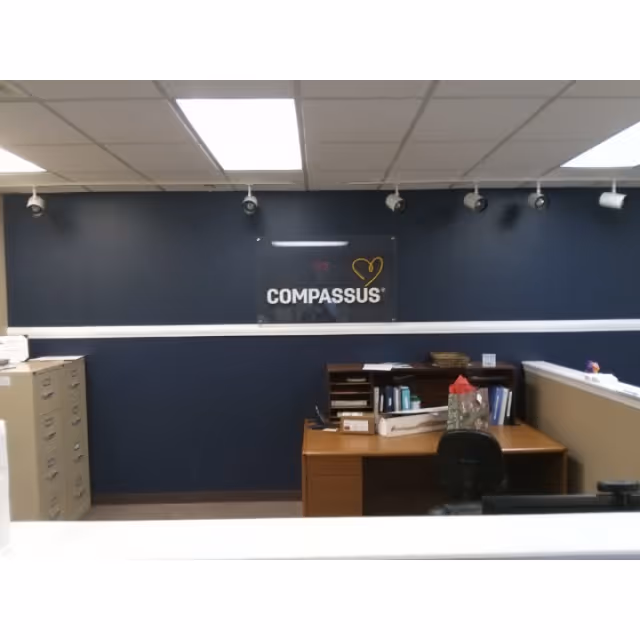 Reception desk area with Compassus sign on dark blue wall.