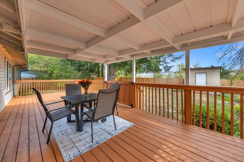Covered wooden outdoor deck with a table, chairs, and a vase of flowers.