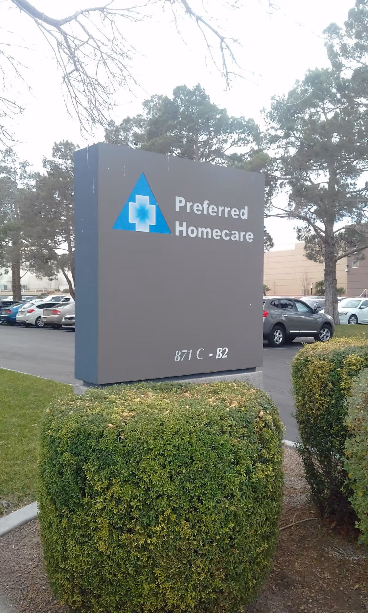 A large gray Preferred Homecare sign with blue logo stands in a parking lot beside hedges.