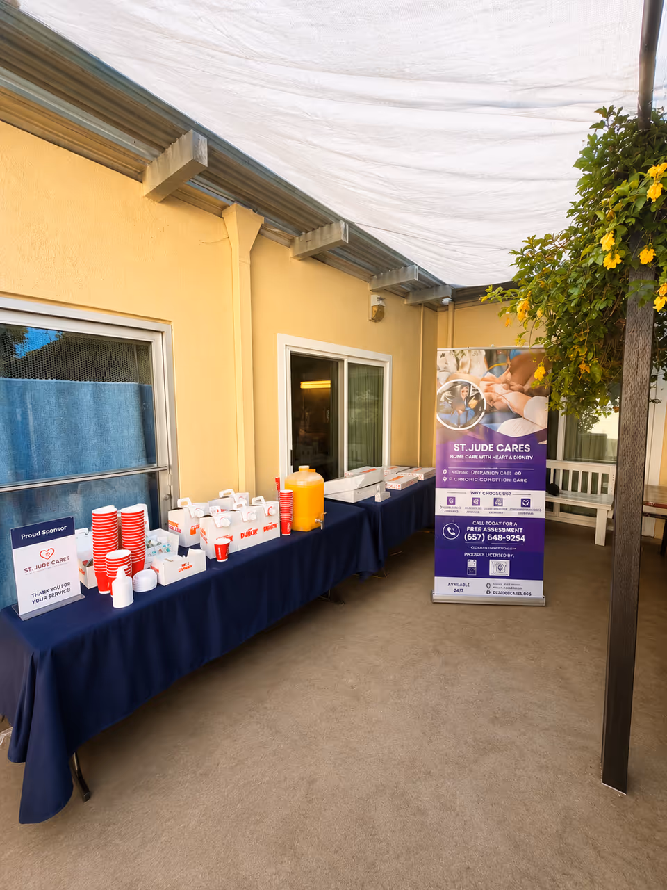 Outdoor service table with cups, snacks, and a ST. JUDE CARES banner by the wall.