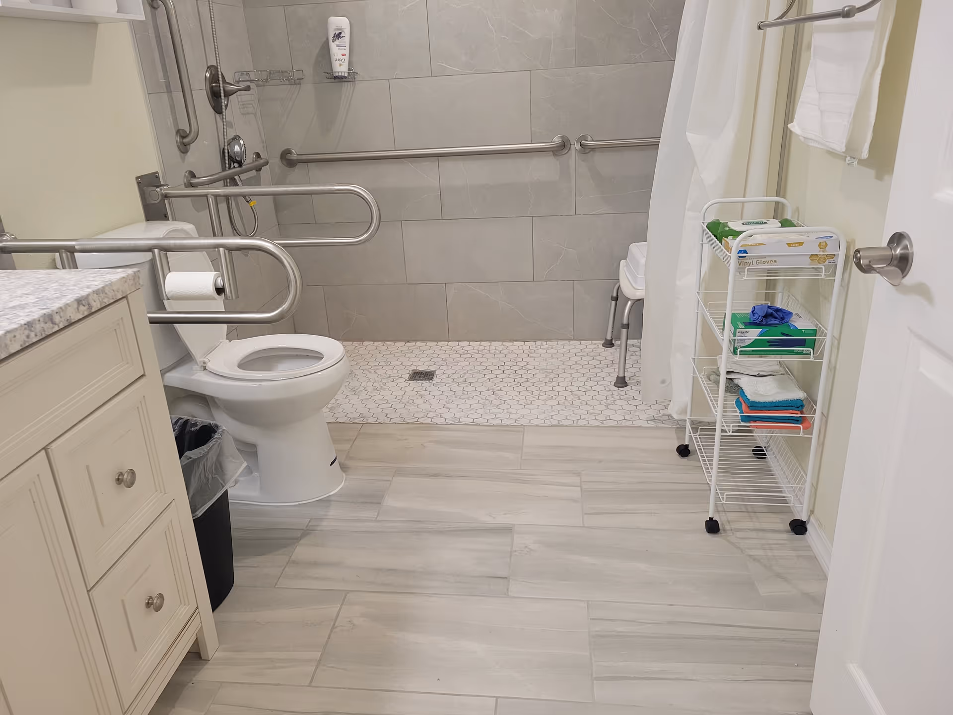 Accessible bathroom in a senior living facility with grab bars, toilet, and a rolling cart.