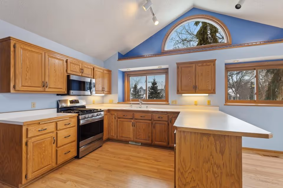 Wooden kitchen with oak cabinets, stainless appliances, and a large arched window.