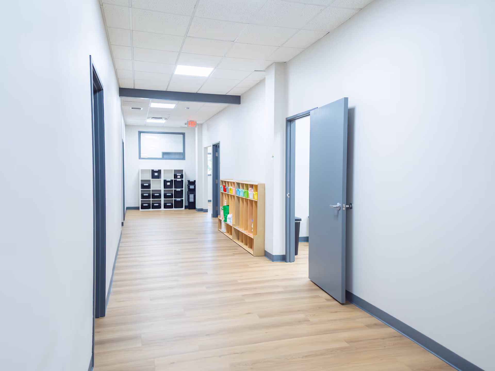 Bright hallway with wood floor, gray doors, and cubbies along the wall.