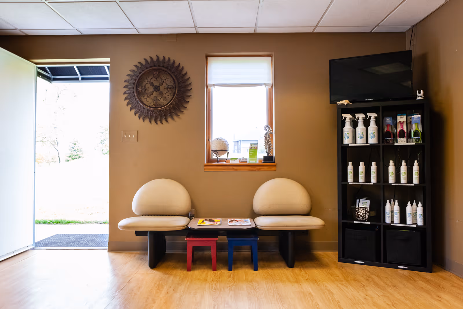 Interior waiting area with two rounded cream chairs, a window, and a tall shelf of products.