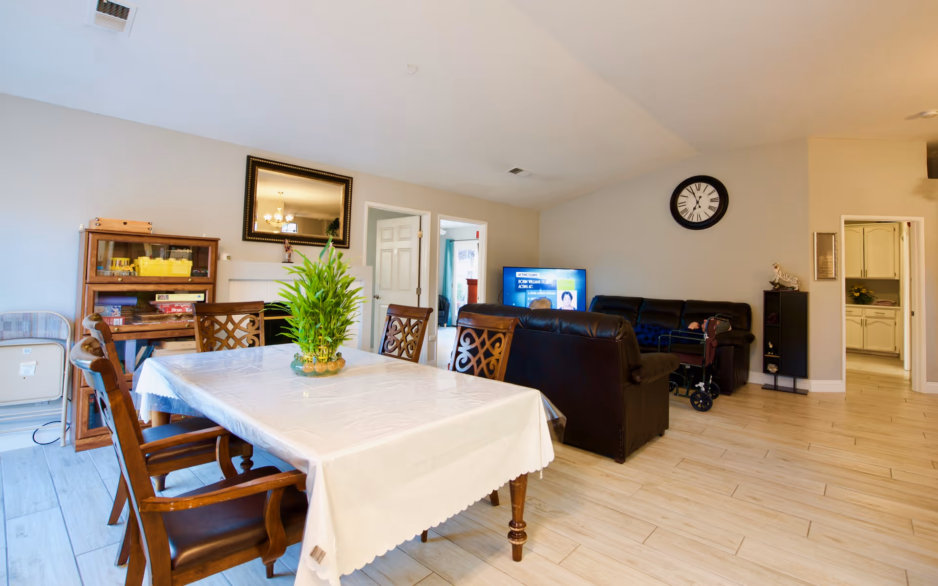 Spacious senior living common area featuring a dining table with plant centerpiece and lounge seating.