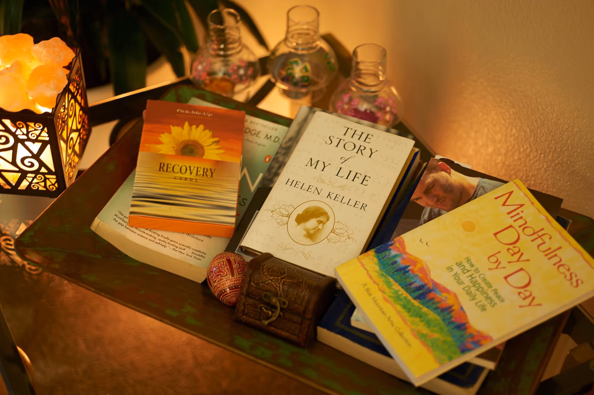 A tabletop with recovery-themed books, a decorative lamp, and trinkets.