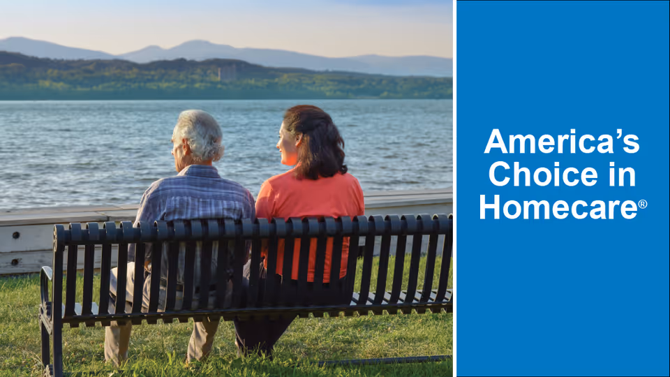 Two elderly people sit on a bench by a lake with a bold blue advertisement panel.