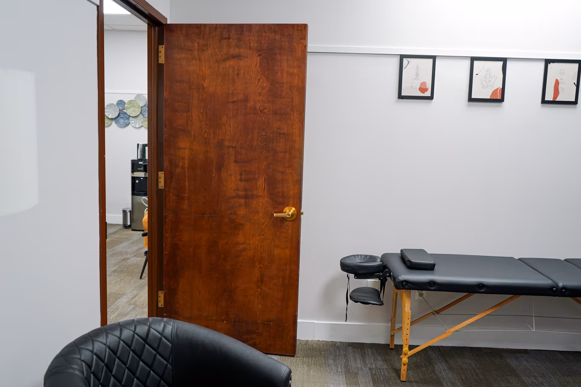 Open wooden door reveals a treatment table in a quiet therapy room.
