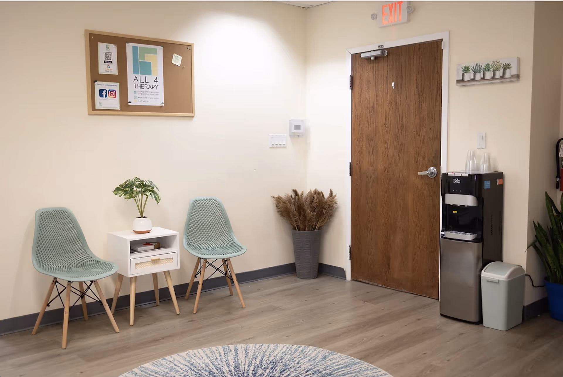 Waiting area with mint chairs, small table, bulletin board, plant, and a water cooler.