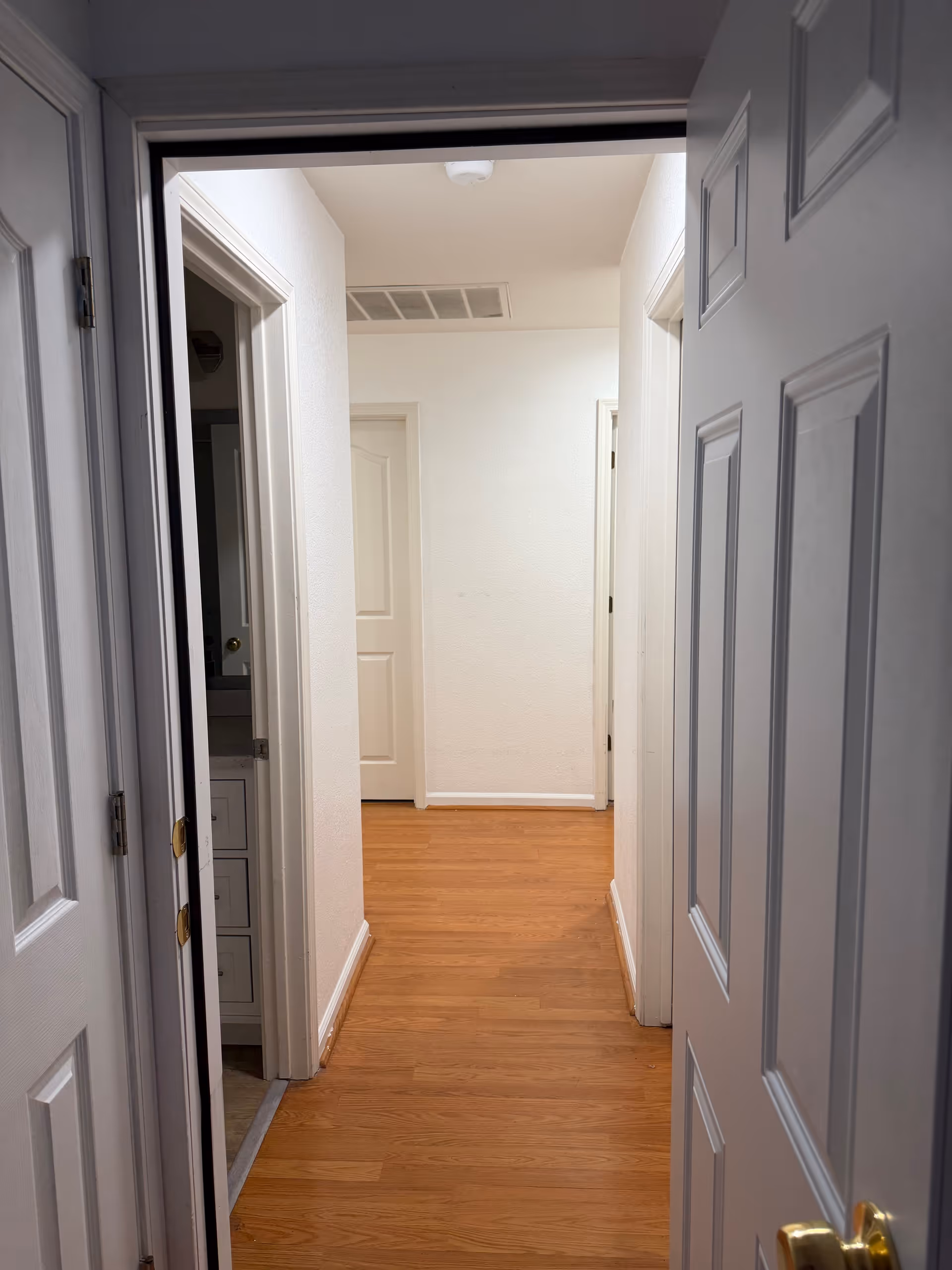 Bright indoor hallway in a senior living facility with white walls and wooden floor.