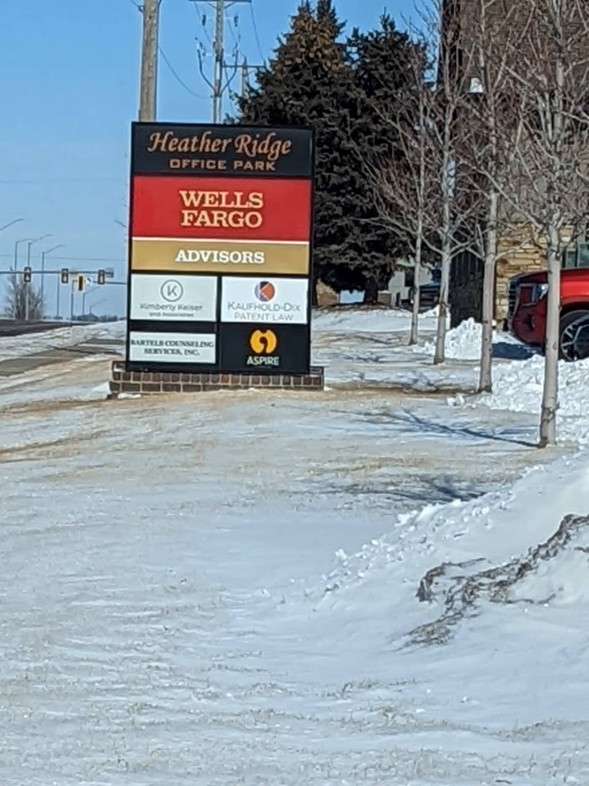 Snowy outdoor signboard displaying multiple business logos in a parking lot.