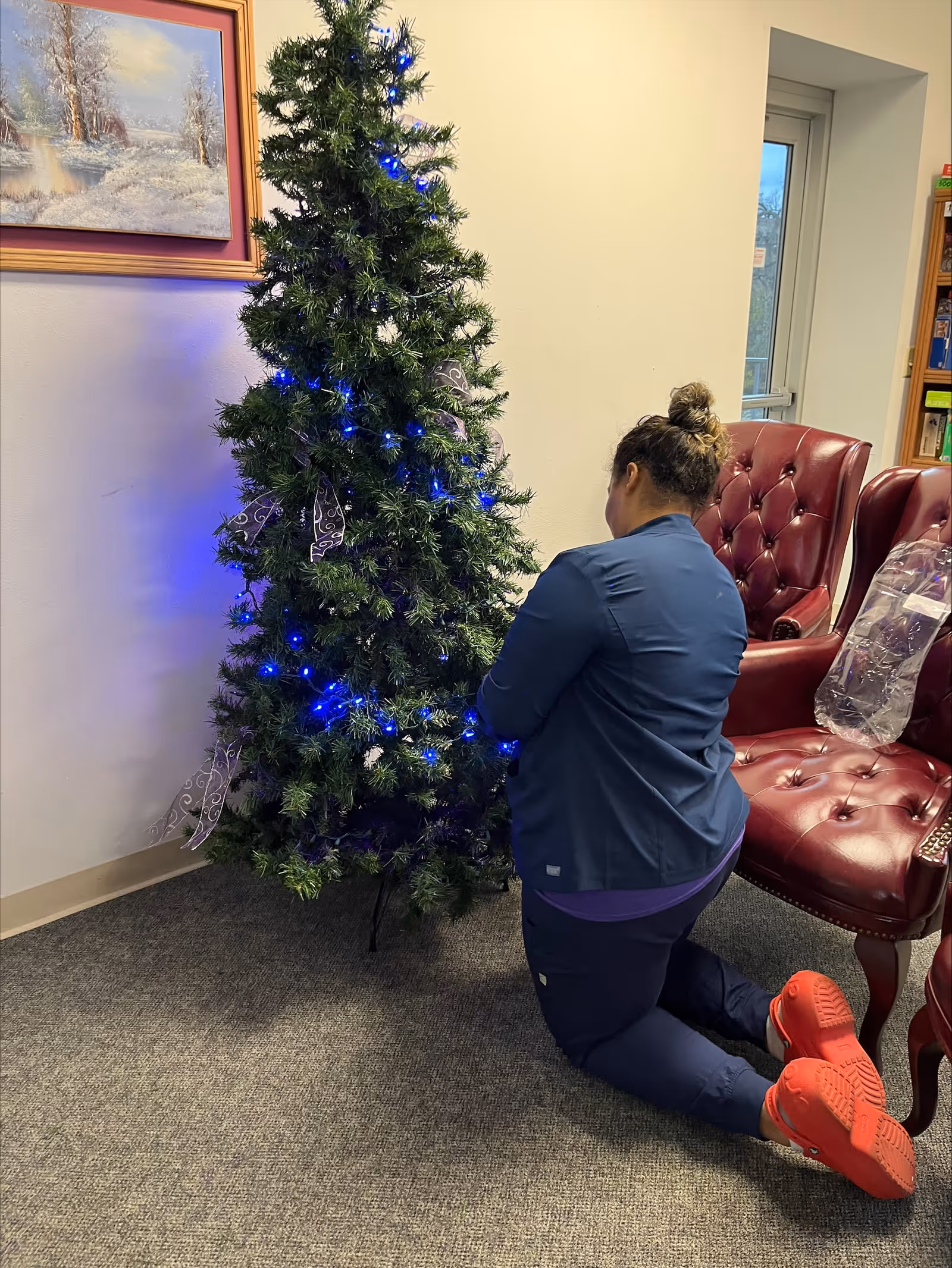 Staff kneels beside a decorated Christmas tree in a cozy indoor lobby.