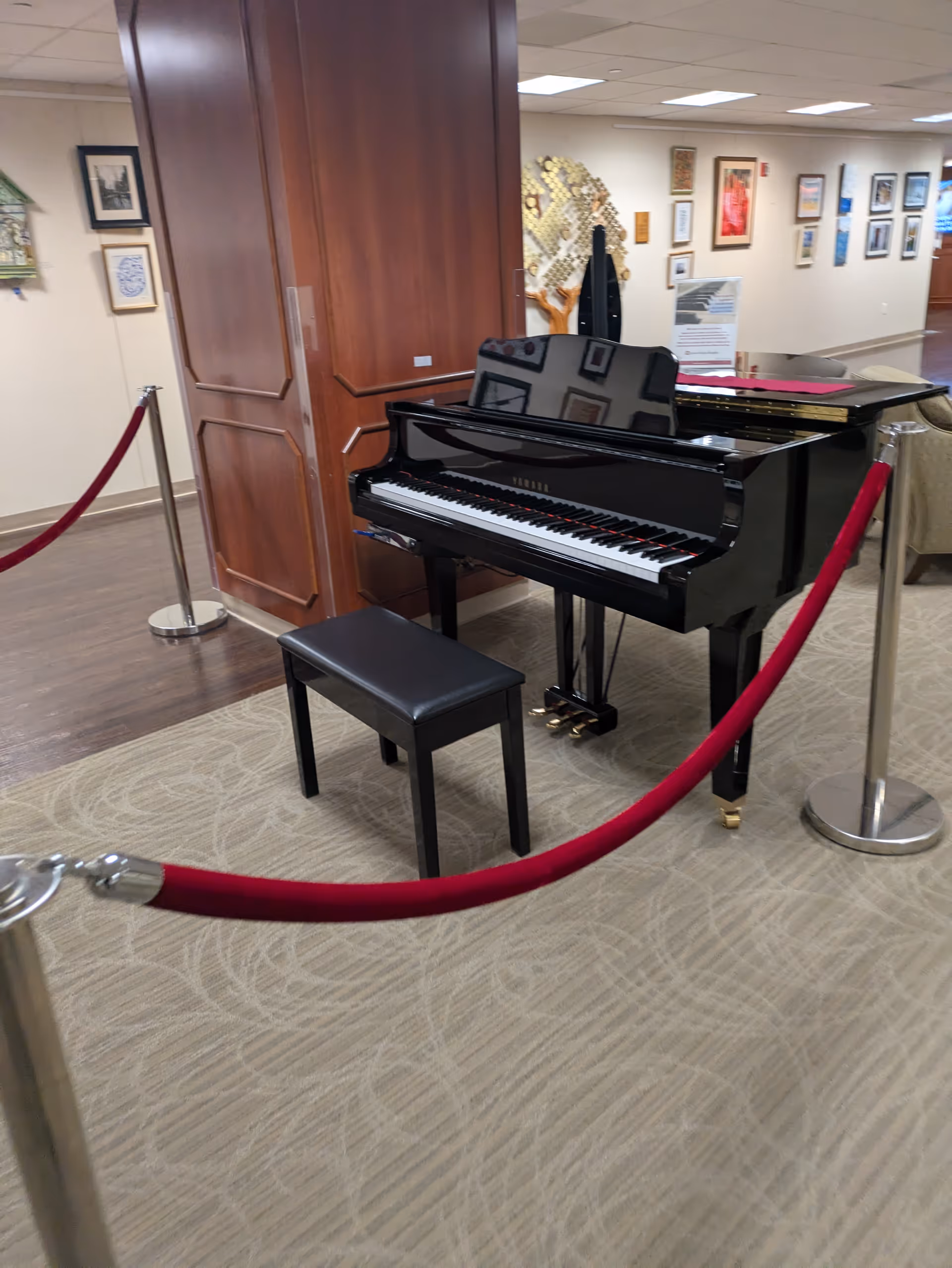 A black grand piano with a bench sits inside a well-lit facility lobby.
