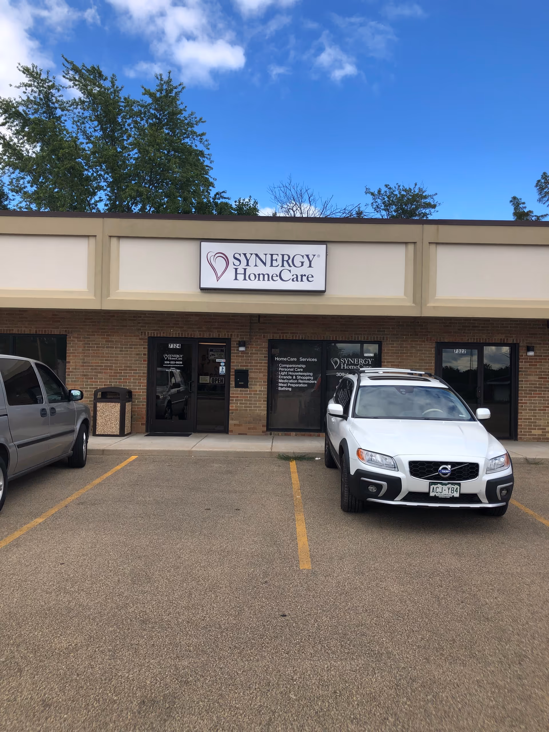 Synergy HomeCare storefront with brick exterior and parked cars in the front lot.