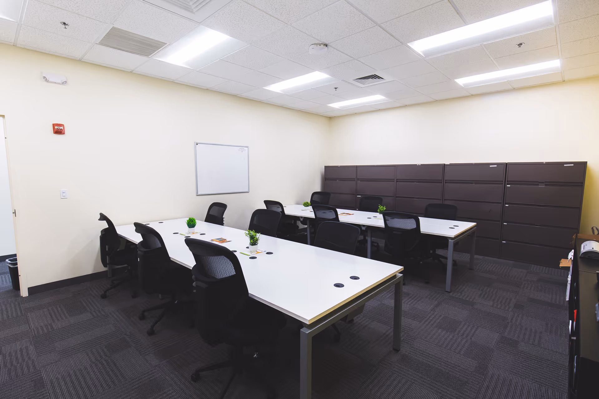 A spacious interior meeting room with white tables, black chairs, whiteboard, and cabinets.