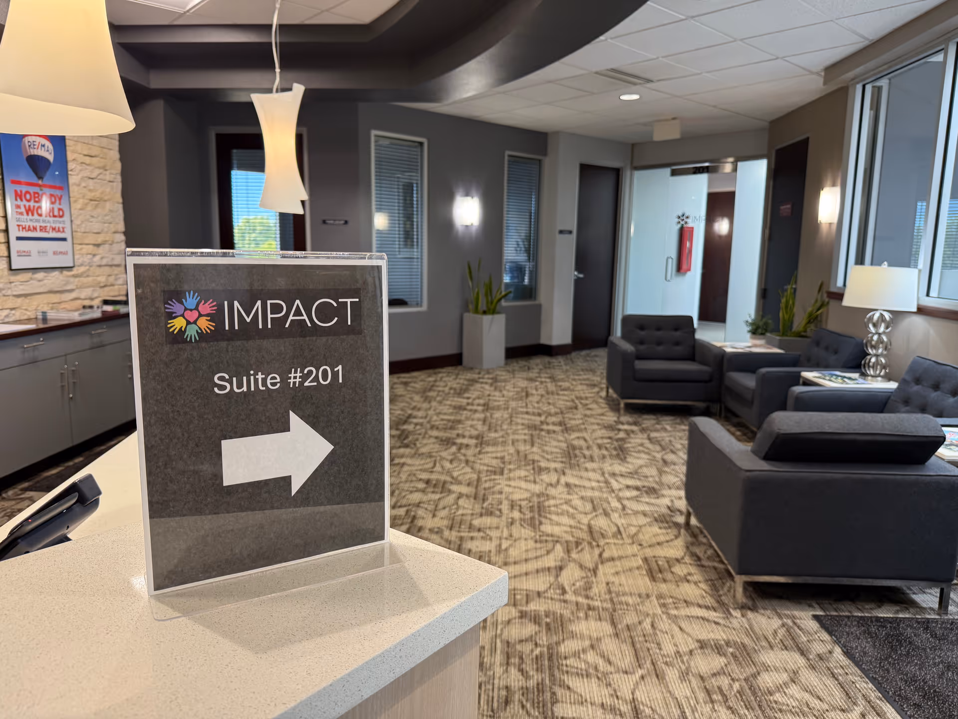 Lobby interior with gray seating, reception desk, and an IMPACT Suite sign with arrow.