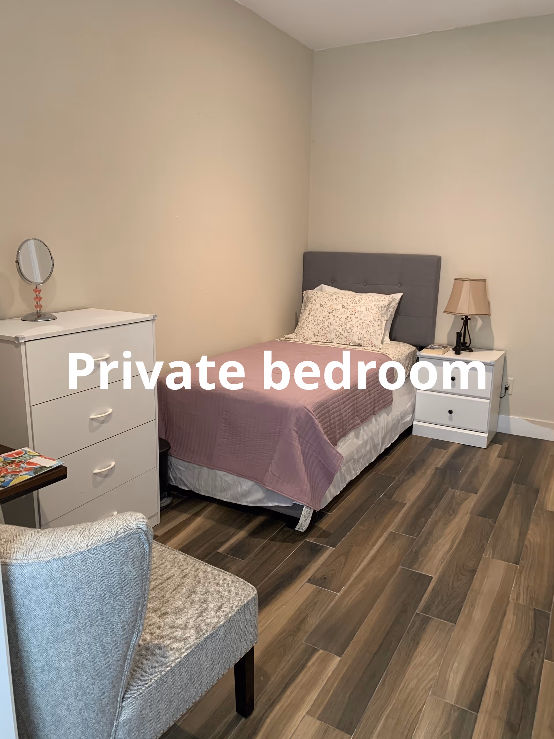 A private bedroom in a retirement home with bed, dresser, nightstand, and chair.