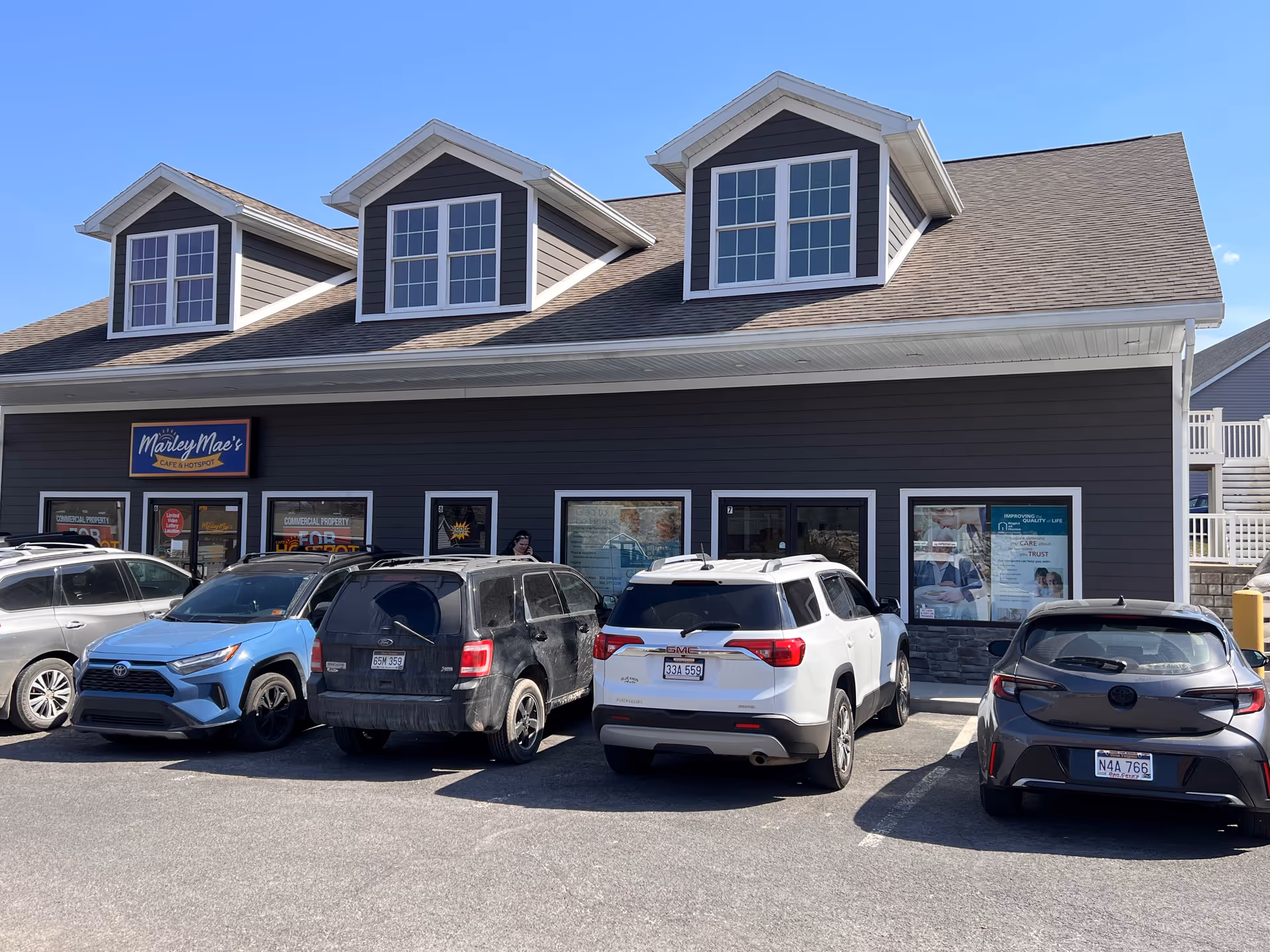 Front of a gray building with three dormer windows and several cars parked outside.