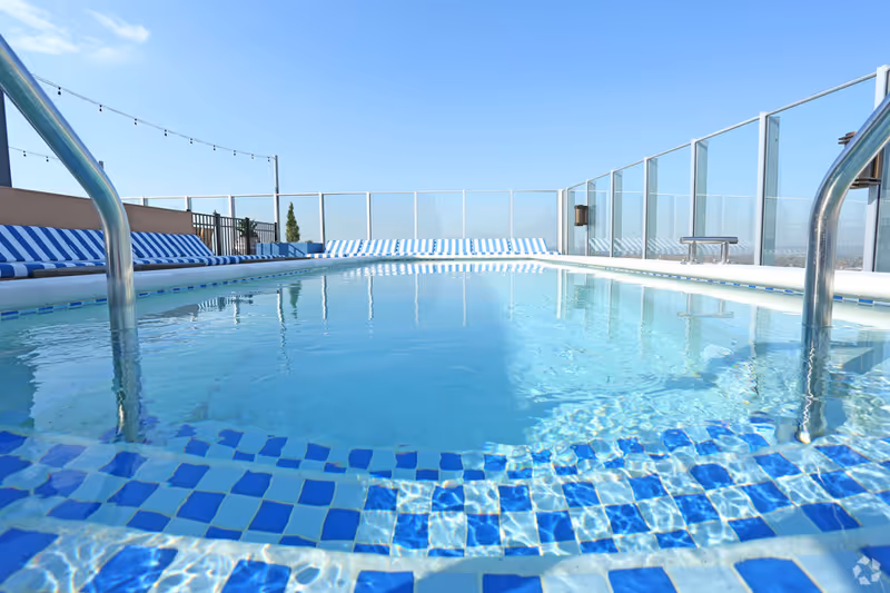 Rooftop outdoor swimming pool with blue-tiled edges and striped lounge chairs.