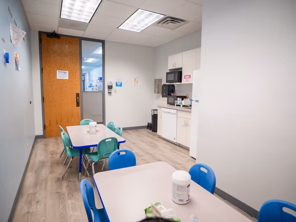 Colorful plastic chairs surround tables in a small dining area with a kitchenette.