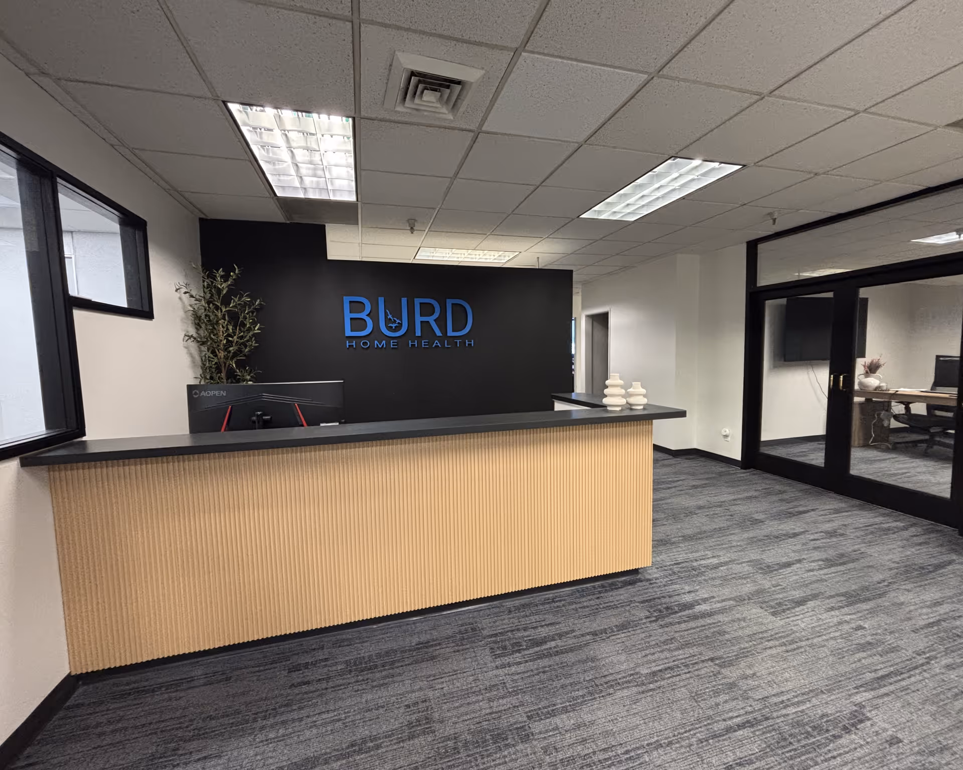 Reception desk in a modern lobby with Burd Home Health sign on dark wall.
