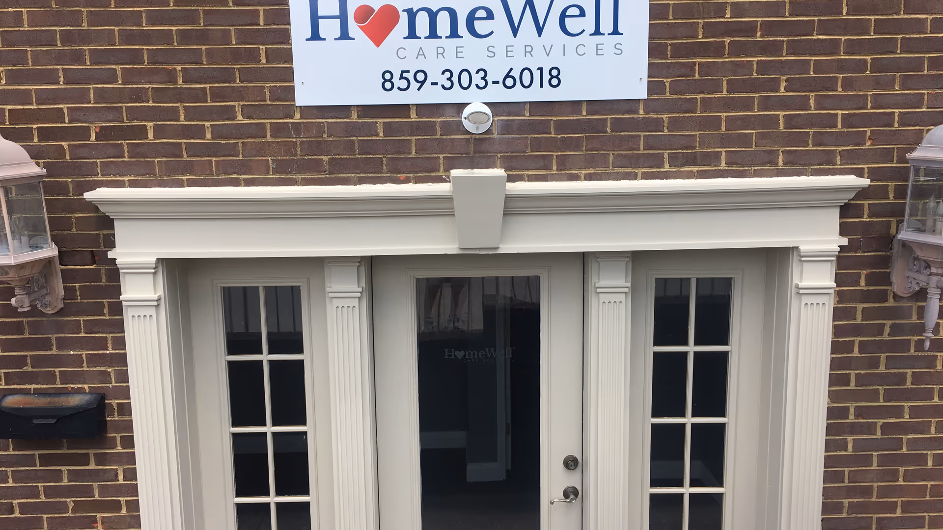 Brick building entrance with a white framed doorway and HomeWell sign overhead.