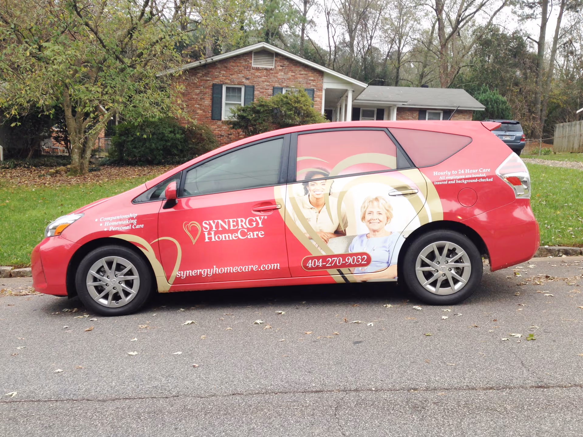 Red Synergy HomeCare van parked on a residential street with a house behind.