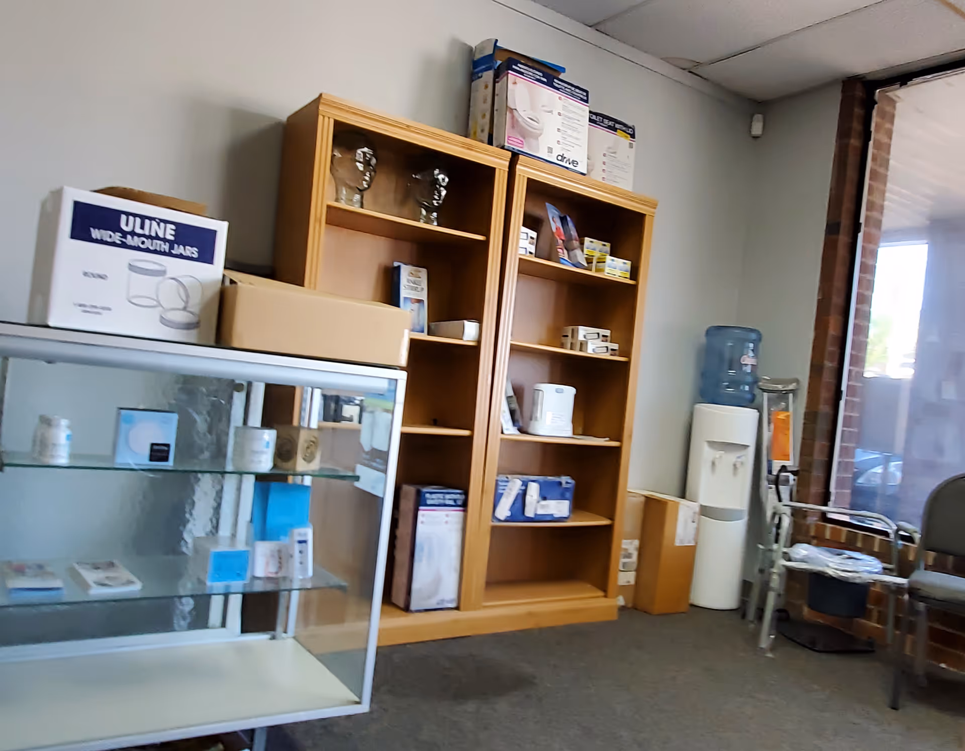 Interior of a facility supply area with shelves, a glass cabinet, and a water cooler.