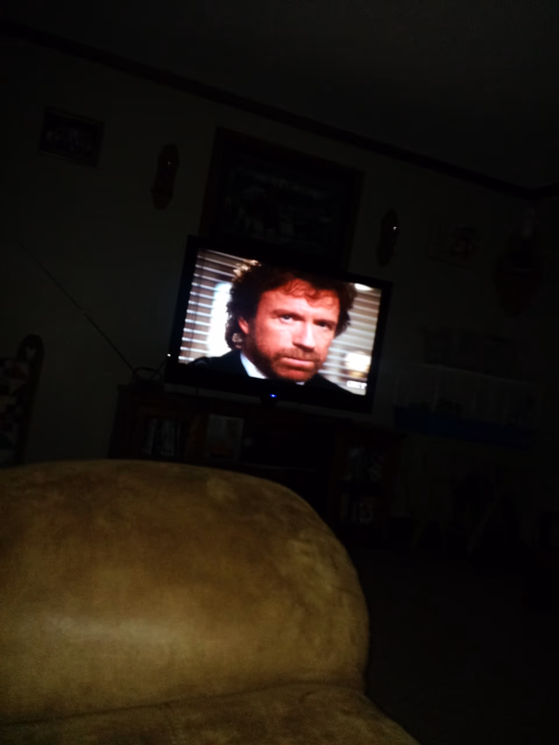 Dim living room with a TV showing a man and a large beige sofa.