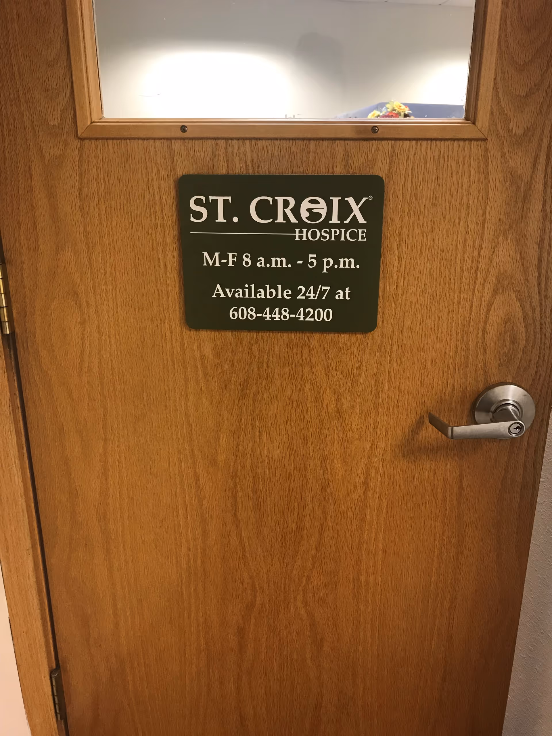 A wooden interior door with a St. Croix Hospice sign and posted hours.