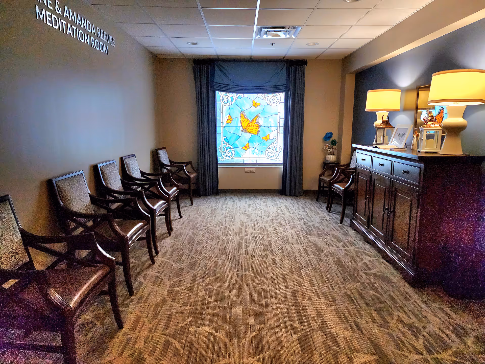 Hallway seating area inside a hospice with a meditation room sign and stained glass window.