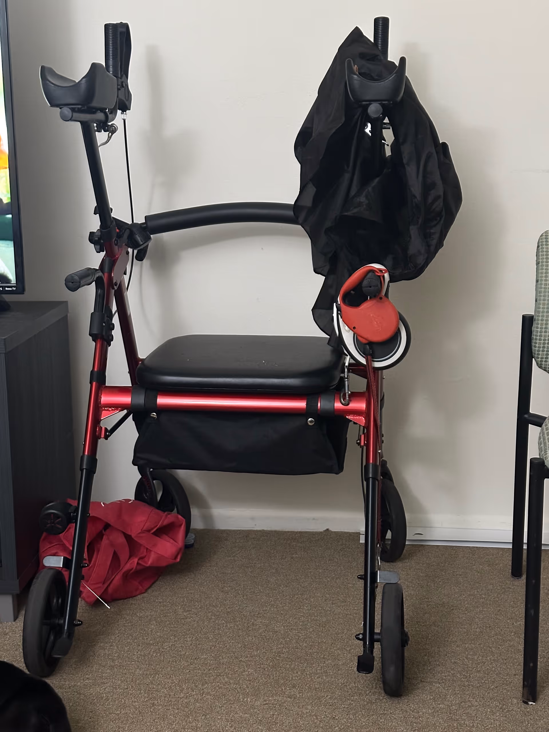 Red mobility walker with a seat and jacket draped over it in a living room.