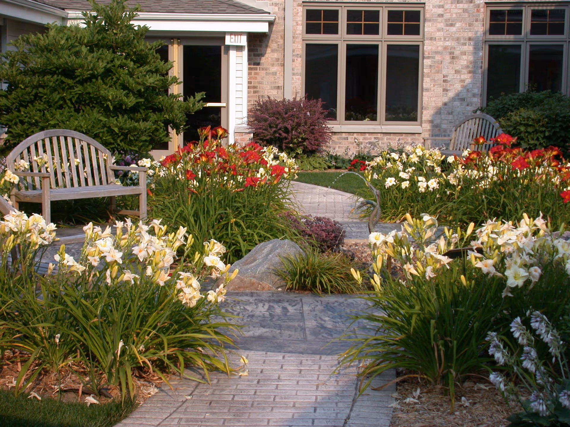 Outdoor garden walkway with blooming flowers, benches, and a brick building facade.