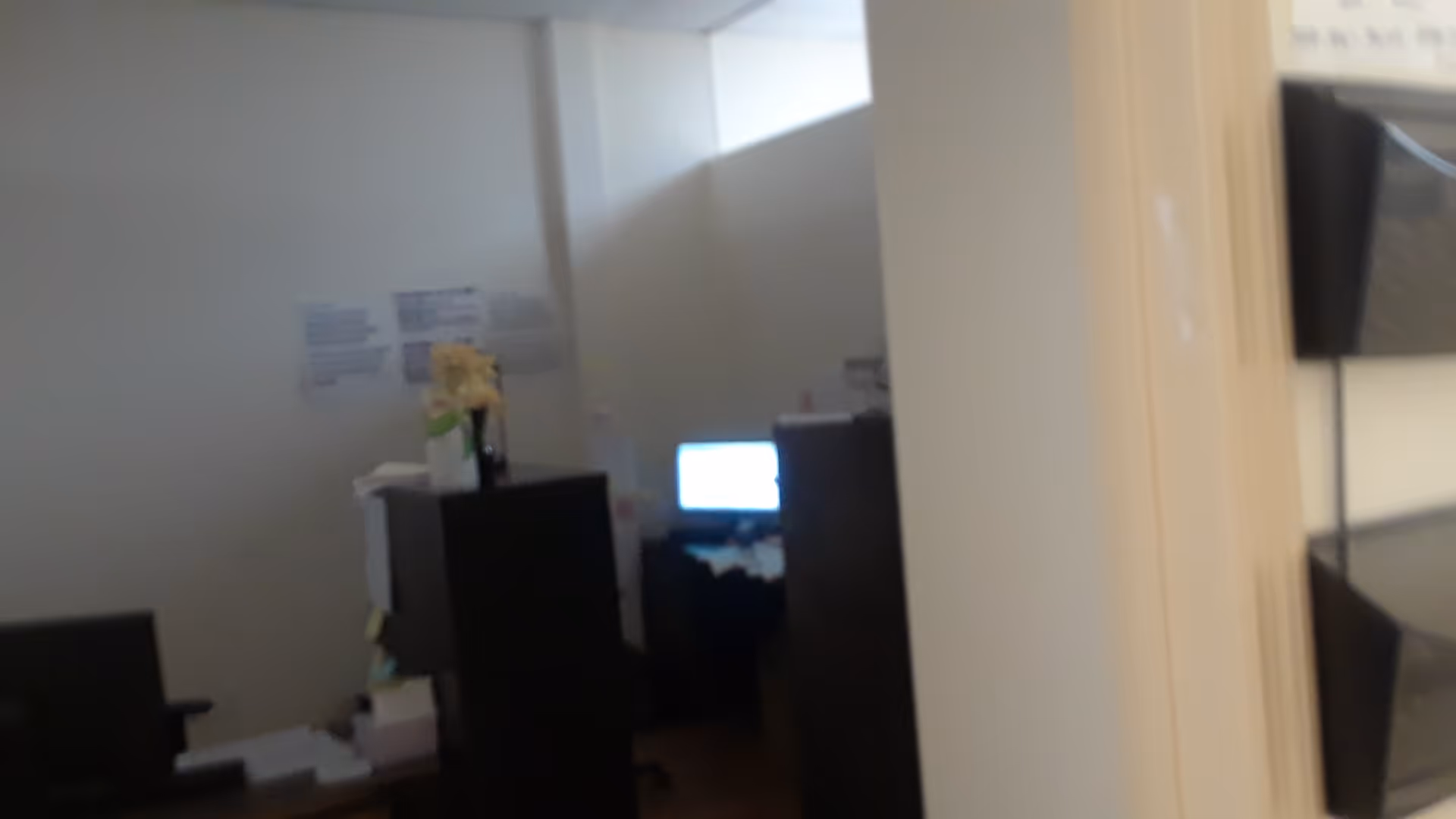 Dim interior office area with desks, computers, and filing cabinets.