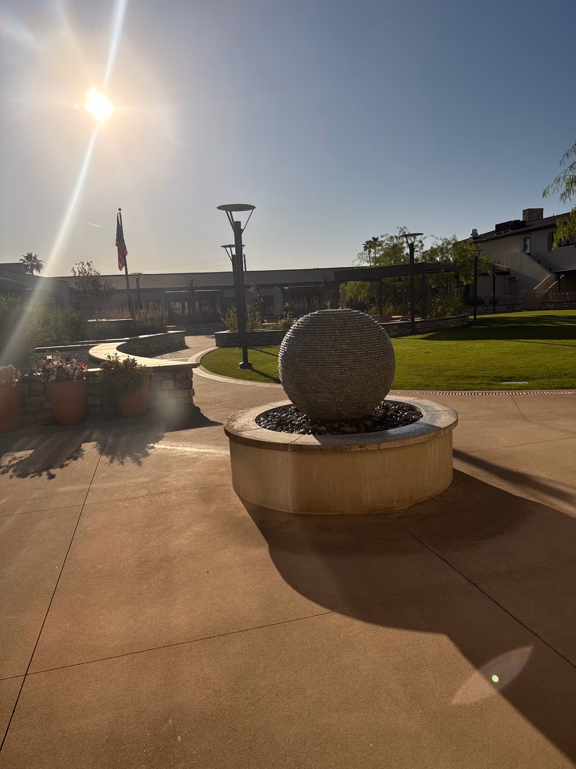 Sunlit courtyard with spherical stone fountain centerpiece and manicured lawn