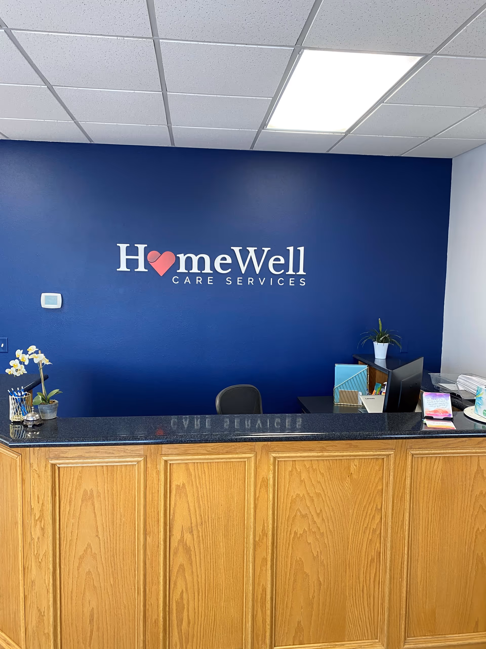 Reception desk in a blue-walled lobby with HomeWell Care Services logo.