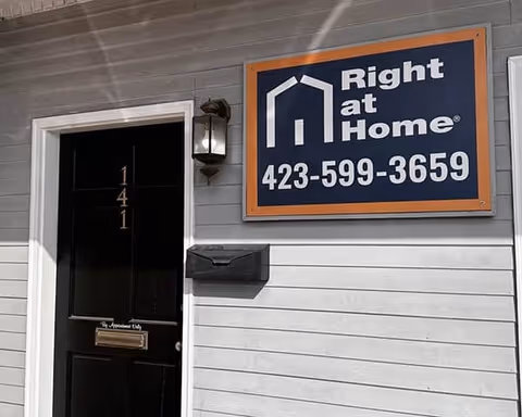 A Right at Home senior living facility sign on the building front beside a black door.
