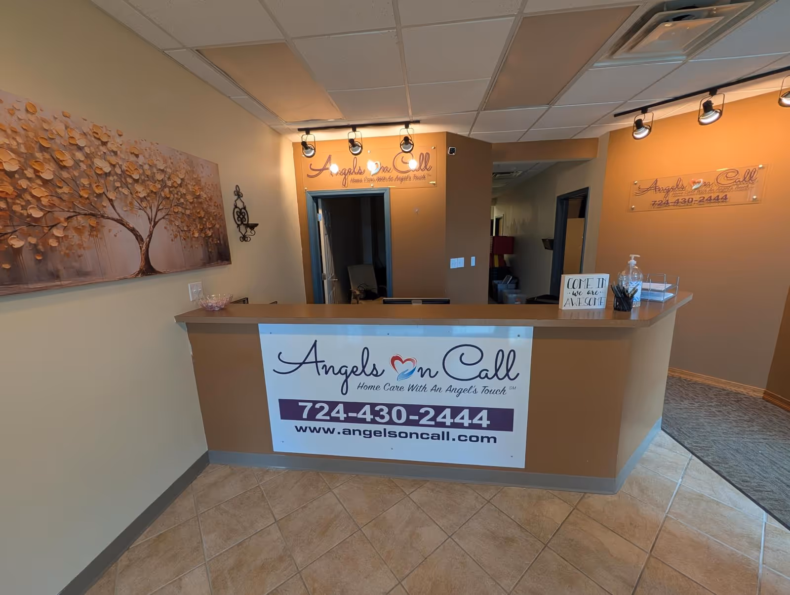 Indoor reception desk with Angels On Call signage, beige walls, and wall art.